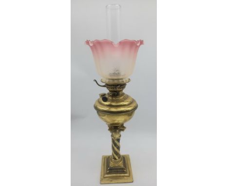 An antique brass column-based oil lamp with pink etched shade complete with chimney.