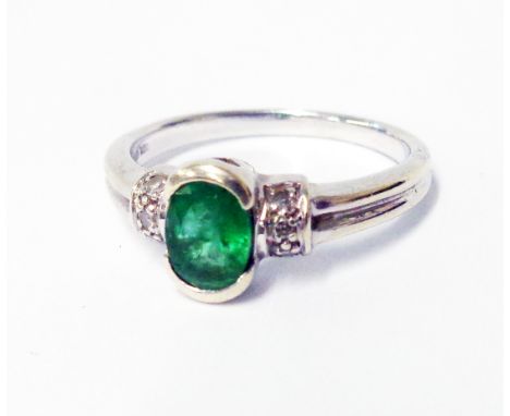 A hallmarked 375 white gold ring, set with central oval emerald and flanking tiny diamonds