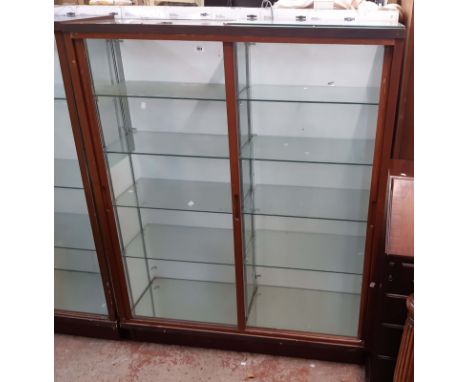 A 1.23m vintage stained wood and glazed shop display cabinet with two banks of shelves enclosed by sliding glazed panel doors