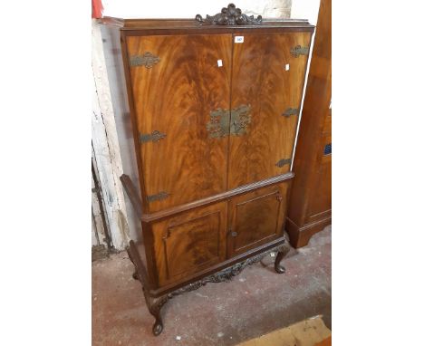 A 85cm vintage flame mahogany veneered drinks cabinet with ornate brass embellishments and strap hinges to pair of doors encl