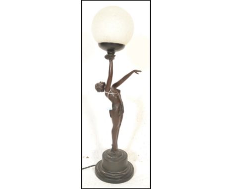 A Art Deco style table lamp in the form of a reclining nude lady holding a frosted glass ball shade atop. Raised on curricula