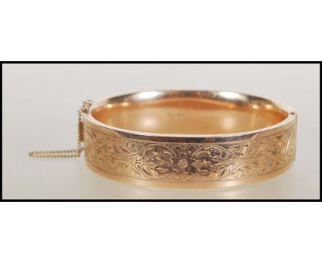 A 9ct gold bangle. The bangle having foliate decoration and hidden clip clasp with safety chain. Assay marks for for South Af