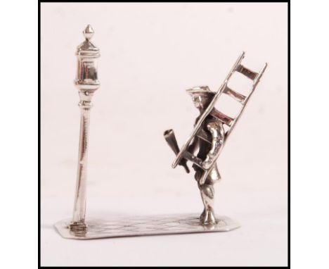 A sterling figurine depicting a lamplighter holder a ladder infront of a street light. Weight 15.9g.&nbsp;