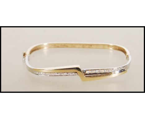 A hallmarked 9ct gold bangle of square form having a crossover of white and yellow gold, set with diamonds to front with figu