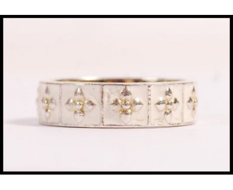 A stamped 925 silver white enamelled fleur de lys style ring, having repeating panels with florals to each. Weight 5.3g. Size