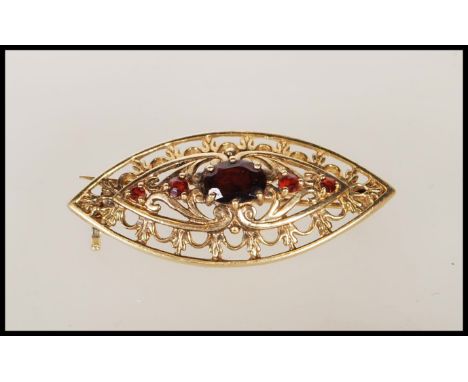 A 9ct gold vintage boat shaped brooch having pierced foliate decoration, set with a central garnet flanked by four smaller ga