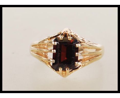 A hallmarked 9ct gold ring claw set with a rectangular cut red stone with reeded shoulders. Hallmarked Birmingham 1999. Weigh