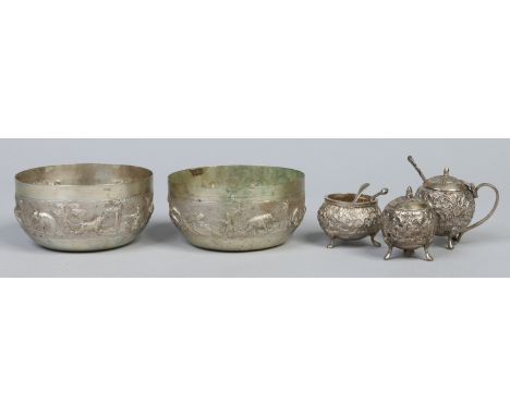 Two Indian white metal repousse work bowls decorated with hunting scenes along with a similar three part cruet. Bowls, 10cm d