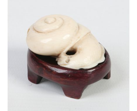 A Japanese Meiji period carved ivory netsuke in the form of a snail and raised on an associated carved hardwood plinth. Signe