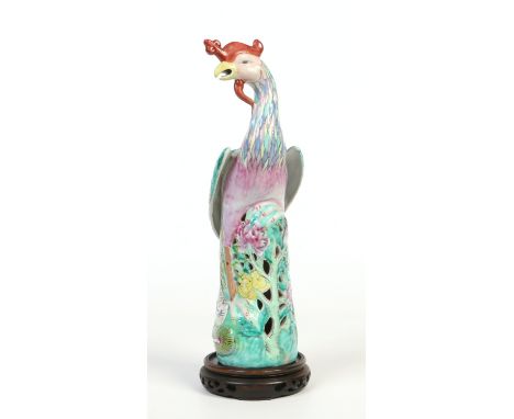 A Chinese famille rose model of a phoenix on a hardwood plinth. Raised on a reticulated base ornamented with peonies, 37.5cm.