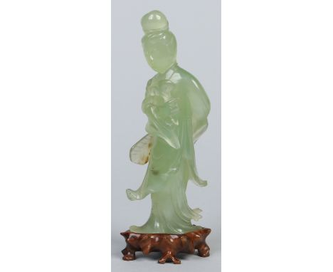 A Chinese carved pale jade figure of Guanyin, holding a ruyi branch and a fan held behind her back in the other hand. Raised 