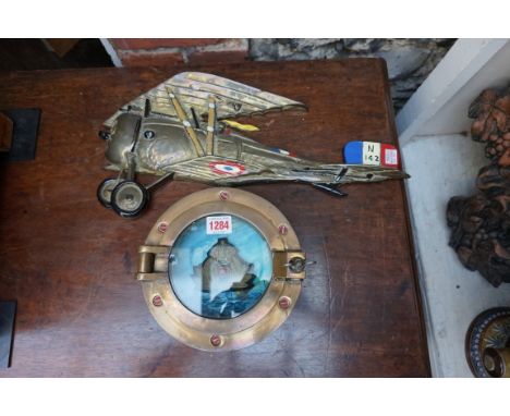 A bronze porthole diorama, 20cm diameter; together with a cast brass and polychrome painted World War I bi-plane plaque, 46.5