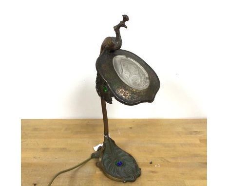 A reproduction aesthetic movement table lamp with a peacock finial above a shield shaped shade with glass insert, on peacock 