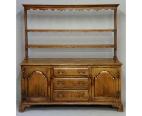 A reproduction oak dresser in early George III style, the flared cornice above a shaped frieze and pair of shaped shelves, th