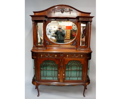 An Edwardian mahogany mirror backed side cabinet, the arched back applied ribbon tied pendants centred on an oval patera, bow