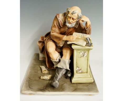 A Naples porcelain figure group by Cortese - The Scribe, the figure seated on a wall writing in a volume leant upon a floral 