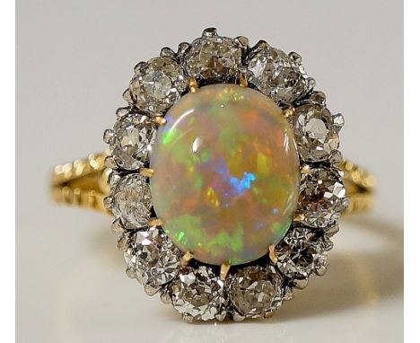 An opal and diamond ring the claw set oval opal within a border of eleven evenly sized diamond brilliants, textured shoulders