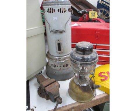 A vintage parafin heater, a tilley lamp and a small bench vice.