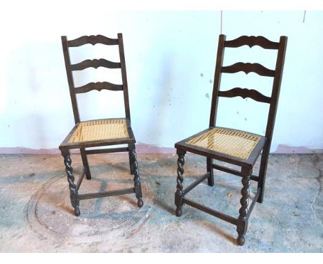 A pair of 1920s/30s oak side chairs with moulded ladder back above caned seats, with barley twist front supports, united by s