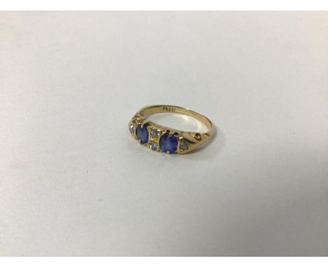 An 18ct gold ring set two blue stones separated by a pair of diamonds and flanked by single diamonds (J) (2.44g)