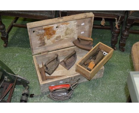 Three flat irons and vintage tools in a pine tool box.