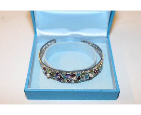 A silver bangle set with various coloured stones