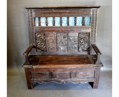 An Oak Settle, the carved and pierced back above a panel seat flanked by stiles, 127cms wide, 47cms deep, 131cms high 