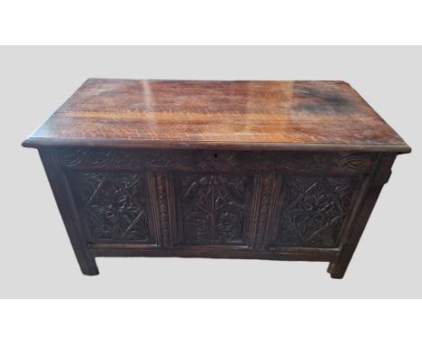 An 18th Century Oak Coffer, the hinged plank top above a carved frieze and three carved panels, the central panel carved with