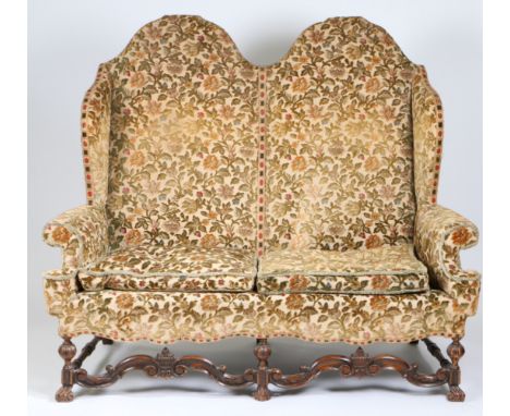 A William & Mary style walnut and upholstered sofa, circa 1900  The double-arched padded back, winged sides, scroll-over arms