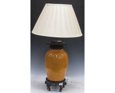 A Chinese lamp, with an ochre glazed pottery body and mounted with a carved hardwood rim, on a hardwood pierced base, with a 