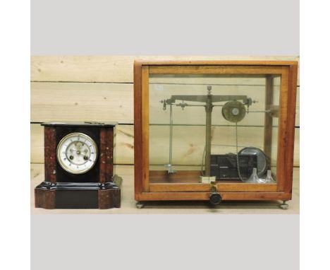 A Victorian black slate mantel clock, together with a set of scales, in a glass display case