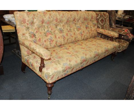 A Victorian upholstered open arm settee with button back, on turned and fluted mahogany supports and legs on brass castors, 1