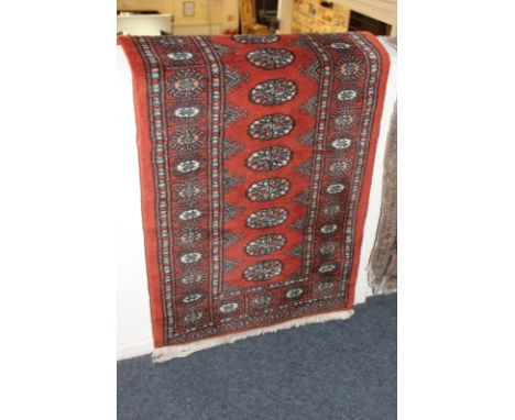 A modern Bokhara carpet, rust coloured ground with single row elephant feet surrounded by border, 350cm by 66cm