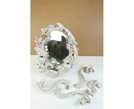 Continental porcelain framed wall mirror, the frame of scrolling form, foliate encrusted and surmounted by a pair of cherubs,