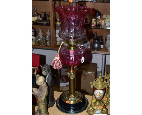 AN EARLY 20TH CENTURY BRASS AND CRANBERRY GLASS OIL LAMP, having Corinthian brass column, cranberry glass reservoir and glass