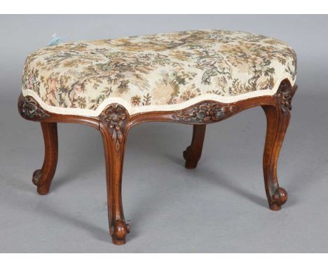 A late 19th century walnut oval stool, the seat overstuffed in a machined tapestry, the frieze carved with flowerheads, on ca
