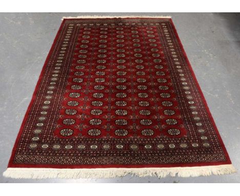 A Pakistan bokhara carpet, late 20th century, the claret field with five columns of guls, within a sunburst gul border, 261cm