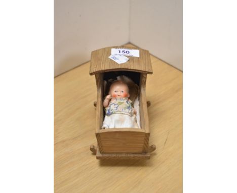 A small ceramic baby inside wooden cot, measures 8cm x 12cm.