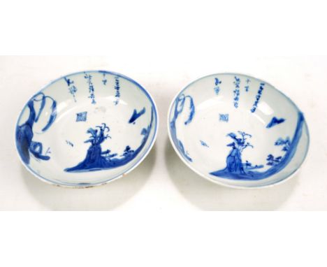 A pair of Chinese porcelain circular bowls painted in underglaze blue with river landscape with boats and trees and with vers