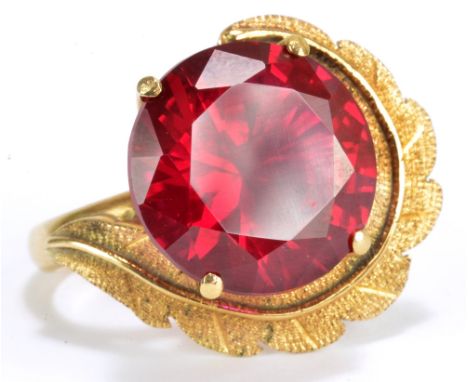 A 14ct yellow gold dress ring set with large vivid red stone with textured swirling leaf beside the four claw mount, size I, 