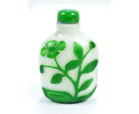 A Chinese Peking green and white carved overlay glass snuff bottle of flat ovoid form decorated with floral motif to each sid