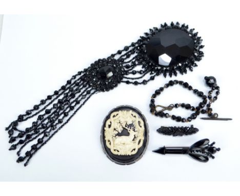 A large oval faceted jet ornament with bead decorated tassels, length 24cm, an arrow shaped brooch, a further example and a b