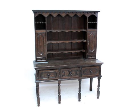 A 20th century oak dresser with boarded rack flanked by two shelves above cupboard doors and small drawers, on base with thre