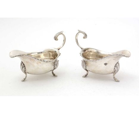 A pair of George V silver sauceboats, on three fluted legs with bobbin borders and leaf-capped, flying scroll handles, by Rei