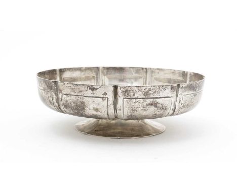 A George V silver bowl, of shallow circular form, on spreading low foot with shield-shaped panels in low relief around the si