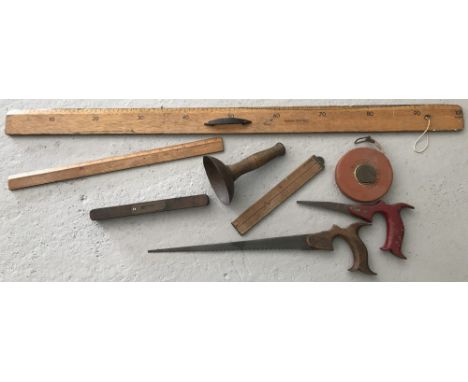 A collection of vintage tools and implements. To include wooden rules, level, tape measure and wooden handled saws. 