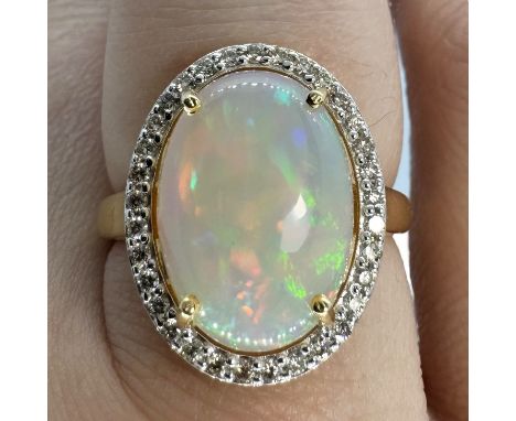 An opal and diamond set cocktail ring. Featuring a 14mm x 10mm cabochon of opal, surrounded by a halo of claw set diamonds to