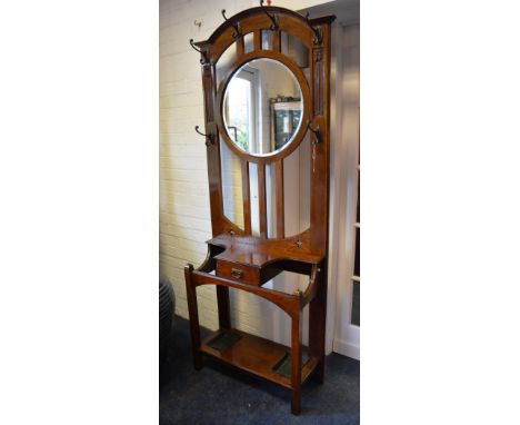 An Arts & Crafts oak hallstand, with metal pegs above circular plate glass mirror, raised on bar supports, above small drawer