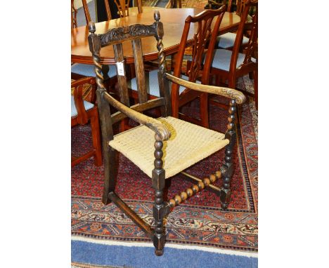 A Jacobean style carved oak open armchair, with bar backs, arm rests ending in scroll terminals, woven seat, raised on bobbin