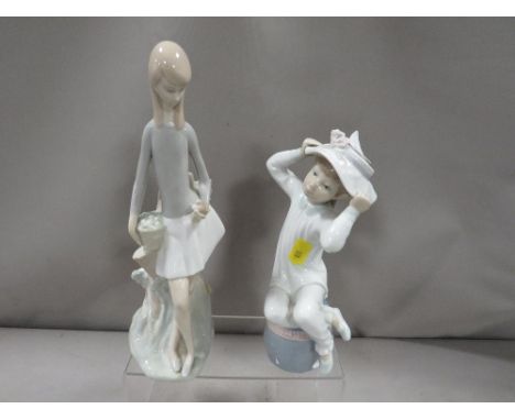 A Lladro figurine of a child trying on a hat together with a Nao figurine of a child holding a bird 